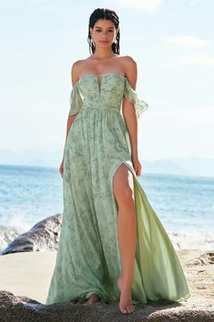 a woman in a green dress standing on the beach with her legs crossed and one leg up