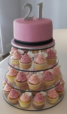 a tiered cake with pink frosting and cupcakes