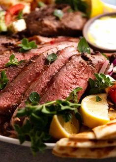 a plate with steak, lemon wedges and salad on it next to some pita bread