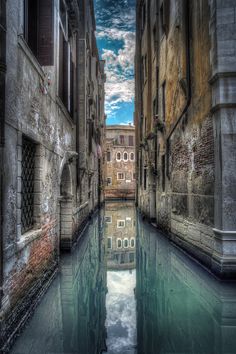 an alley way with water in it and buildings on both sides, reflecting the sky