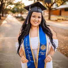 a woman wearing a blue and gold graduation cap and gown standing on the side of a road