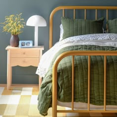 a bed with green sheets and pillows next to a night stand on a checkered rug