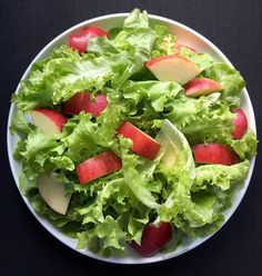 an apple and lettuce salad on a white plate with red apples in it