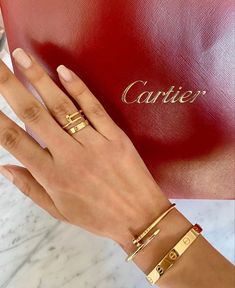 a woman's hand with two gold bracelets on her wrist and a red purse