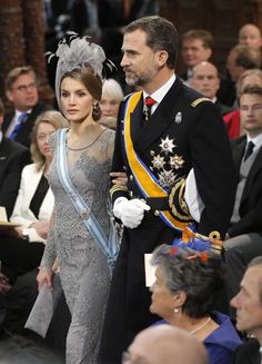 a man and woman dressed in formal attire walking down the aisle with other people watching