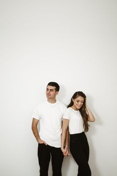 a man and woman standing next to each other in front of a white wall holding hands