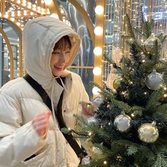 a woman in a white jacket standing next to a christmas tree