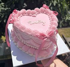 a heart shaped cake with pink icing and ribbon