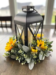 a lantern with sunflowers and greenery sits on a table