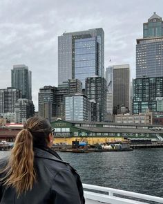 a woman is looking out over the water in front of some tall buildings and skyscrapers