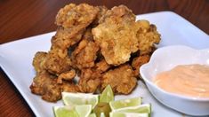 some fried food on a white plate with lime wedges and sauce in a bowl