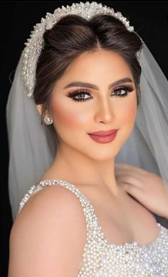 a woman in a wedding dress wearing a veil and pearls on her head is posing for the camera