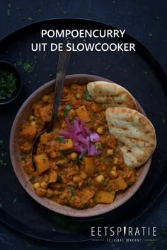 a bowl filled with stew next to pita bread on top of a black plate