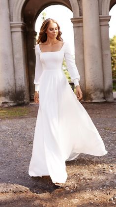 a woman in a long white dress is walking through an old building with arches and archways