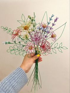 a person holding a bunch of flowers made out of string and paper with scissors in their hand