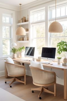 two computer screens sitting on top of a wooden desk in front of three large windows