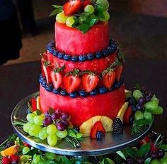 a three tiered cake with fruit on top and grapes, strawberries, blueberries, oranges, raspberries