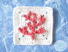 a crocheted square with a red flower on the front and bottom, sitting on a blue surface