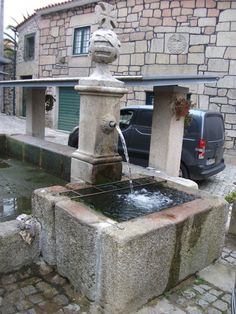 a water fountain in the middle of a cobblestone street next to a car