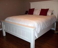 a large white bed with red pillows on it's headboard and foot board