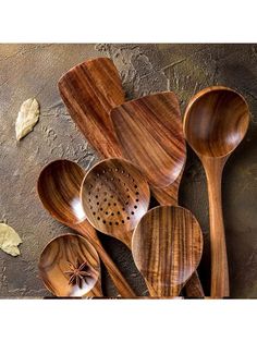 wooden spoons and spatulas are arranged on a stone counter top, with leaves scattered around them