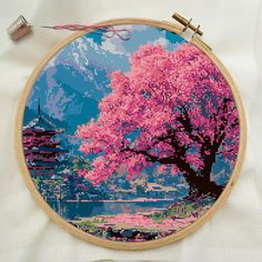 a cross stitched picture of a tree with pink flowers in front of a mountain