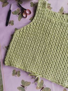 a crocheted green top next to scissors and flowers