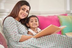 a woman sitting next to a child on top of a couch holding an open book