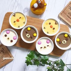 four desserts are arranged in small bowls on a wooden tray next to a potted plant