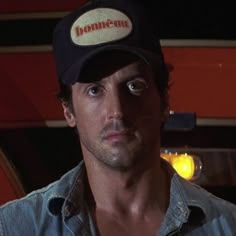 a man in a denim shirt and hat looking at the camera with an intense look on his face