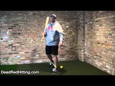 a man holding a baseball bat standing next to a ball in a room with brick walls