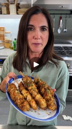 a woman holding a plate full of chicken skewers on a kitchen counter top