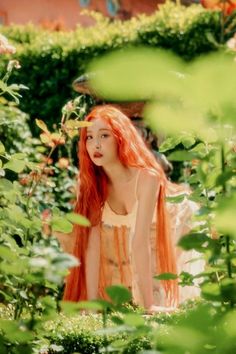 a woman with long red hair is standing in the bushes