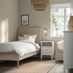 a white bed sitting next to a window on top of a wooden floor in a bedroom