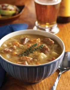 there is a bowl of soup on the table next to a glass of beer and a spoon