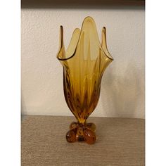 a yellow vase sitting on top of a table next to a white wall and brown carpet