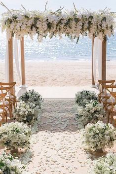 an outdoor wedding setup on the beach with white flowers and greenery in front of it