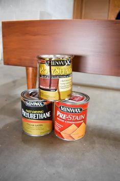 three cans of paint sitting on top of a wooden bench