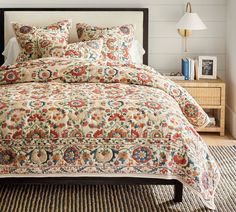 a bed with a floral comforter on top of it in a room next to a lamp