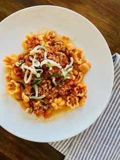 a white plate topped with pasta covered in meat and sauce on top of a wooden table