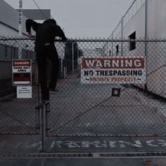 a man standing on top of a metal fence next to a no trespassing sign