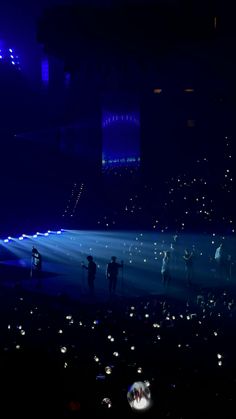 a group of people standing on top of a stage under blue lights in the dark