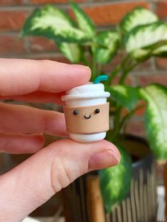 a hand holding a small cup with a smiley face on it and a green plant in the background