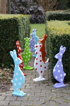 several colorful bunny statues sitting on top of a brick walkway in front of some bushes