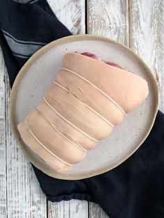 a white plate topped with sliced meat on top of a black cloth next to a wooden table