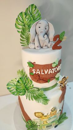 a three tiered cake decorated with an elephant and jungle scene on it's side