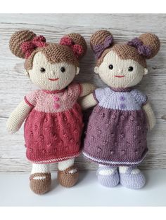 two knitted dolls standing next to each other on a white surface with wood planks