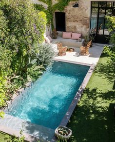 an outdoor swimming pool surrounded by greenery and furniture in a backyard area with patio furniture