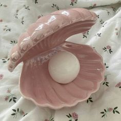 a pink shell with an egg in it sitting on a floral print bed sheet, next to a white ball