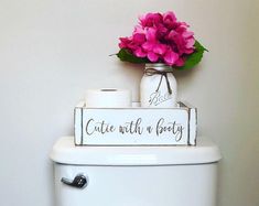 a white toilet sitting next to a pink flower in a vase on top of it